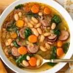 A white bowl is filled with rich white bean and sausage soup.