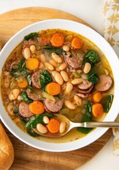 A white bowl is filled with rich white bean and sausage soup.