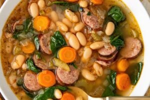 A white bowl is filled with rich white bean and sausage soup.