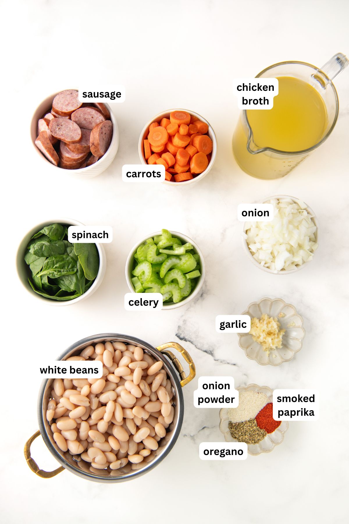 Ingredients for crockpot white bean and sausage soup recipe in order from top to bottom: sausage, carrots, chicken broth, spinach, celery, onion, garlic, white beans, onion powder, oregano, smoked paprika.