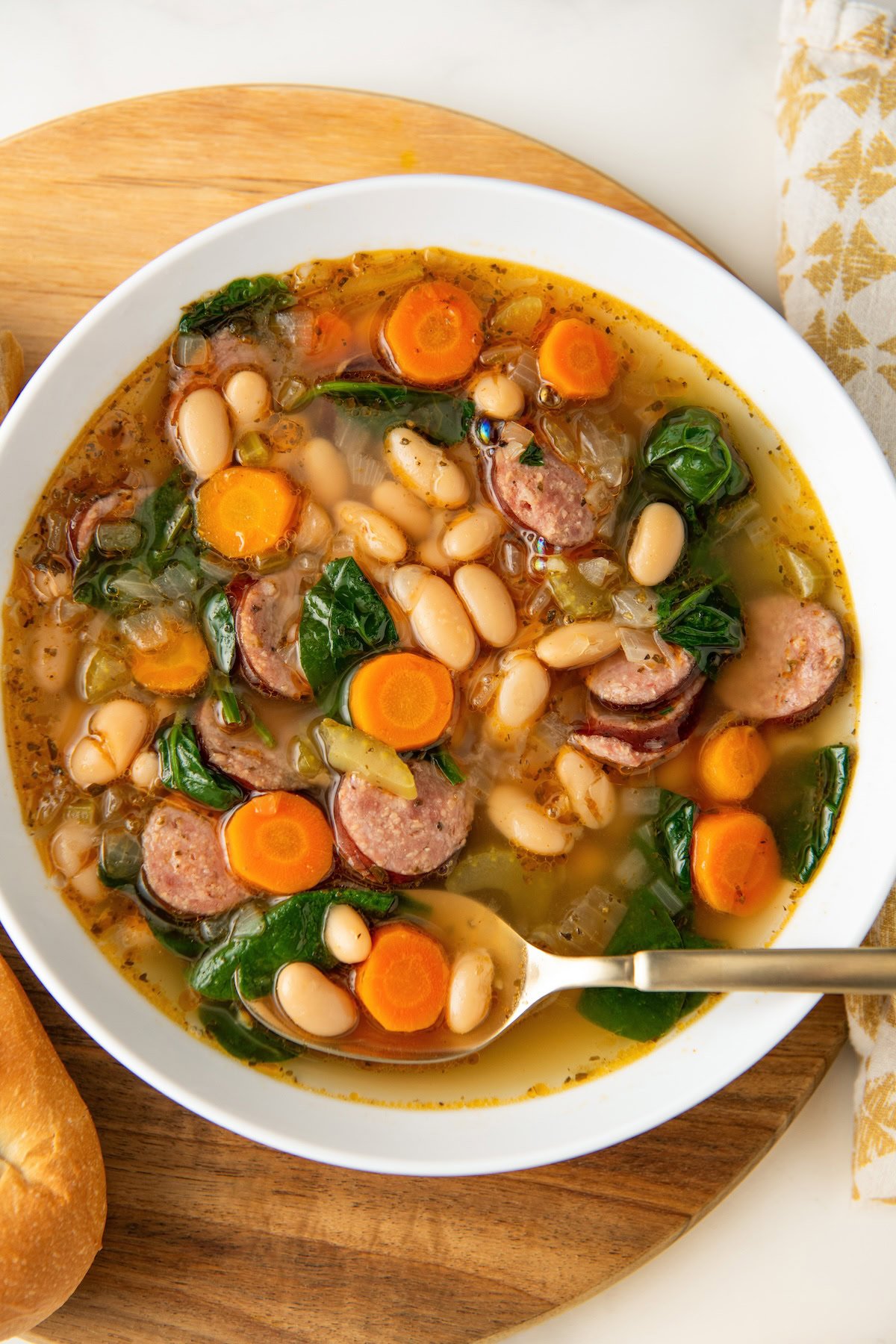 A white bowl is filled with rich white bean and sausage soup.