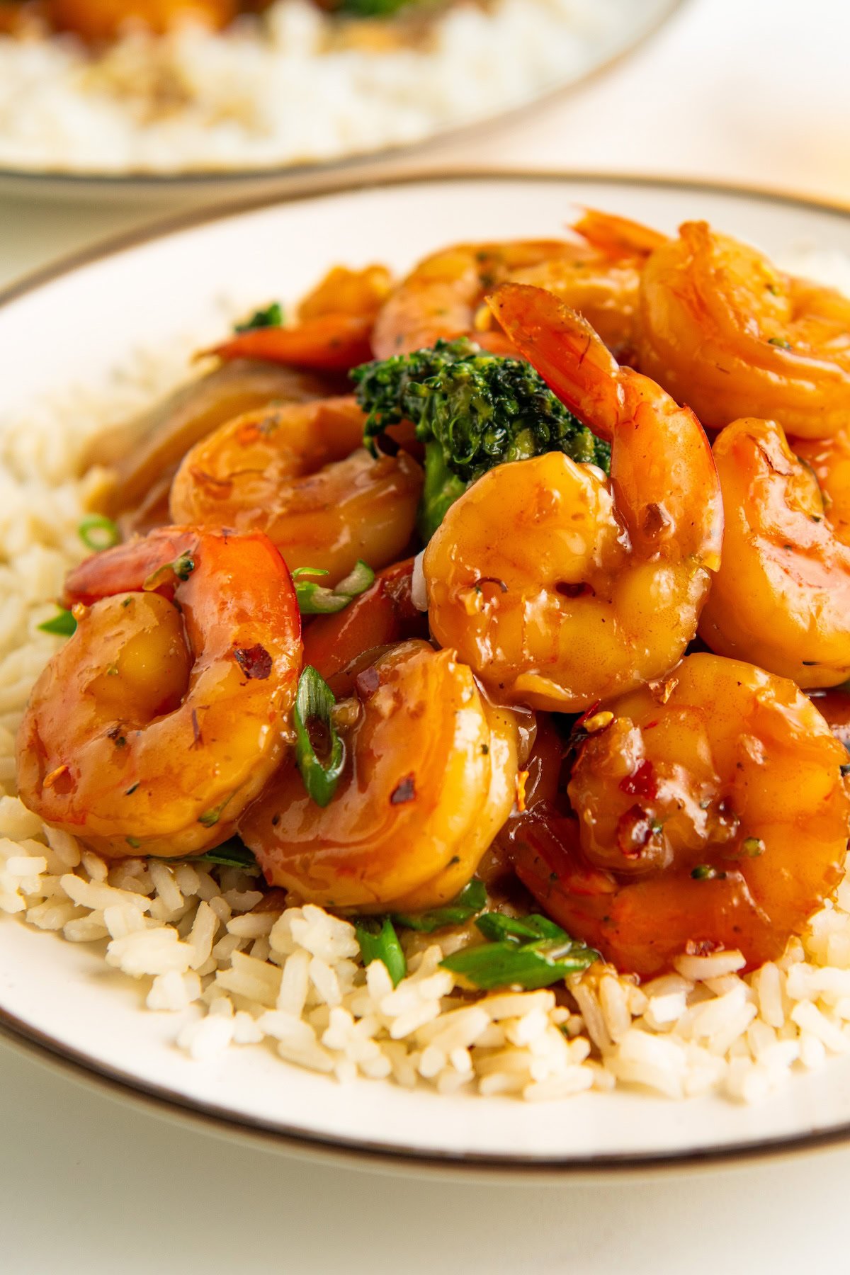 Honey garlic shrimp and broccoli is served over rice on a white plate.