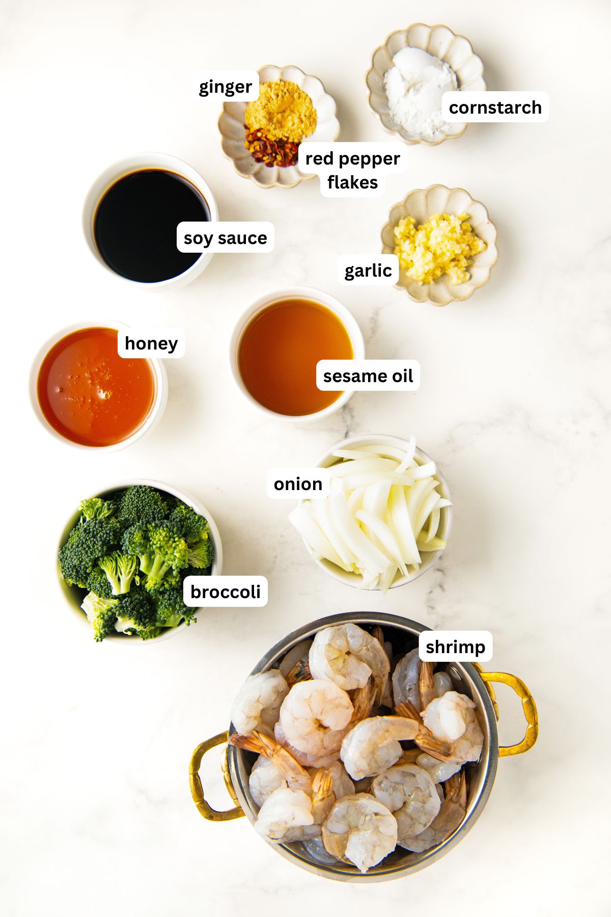 The ingredients for honey garlic shrimp recipe in order from top to bottom: cornstarch, ginger, red pepper flakes, soy sauce, garlic, honey, sesame oil, onion, broccoli, shrimp.