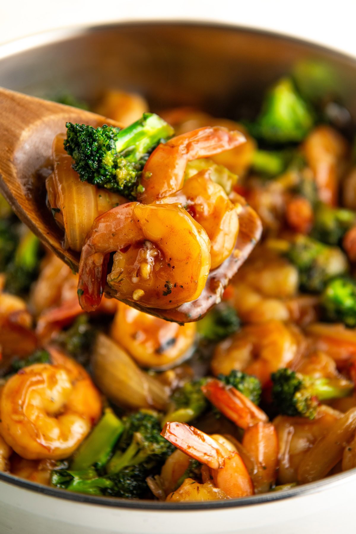 A small portion of honey garlic shrimp with broccoli is being lifted from a skillet.