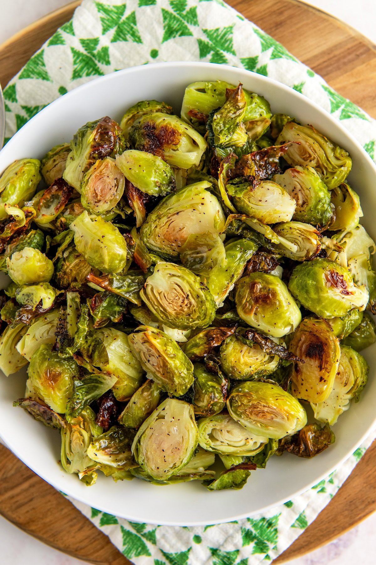 A large serving of fully cooked brussels sprouts are presented in a white bowl.