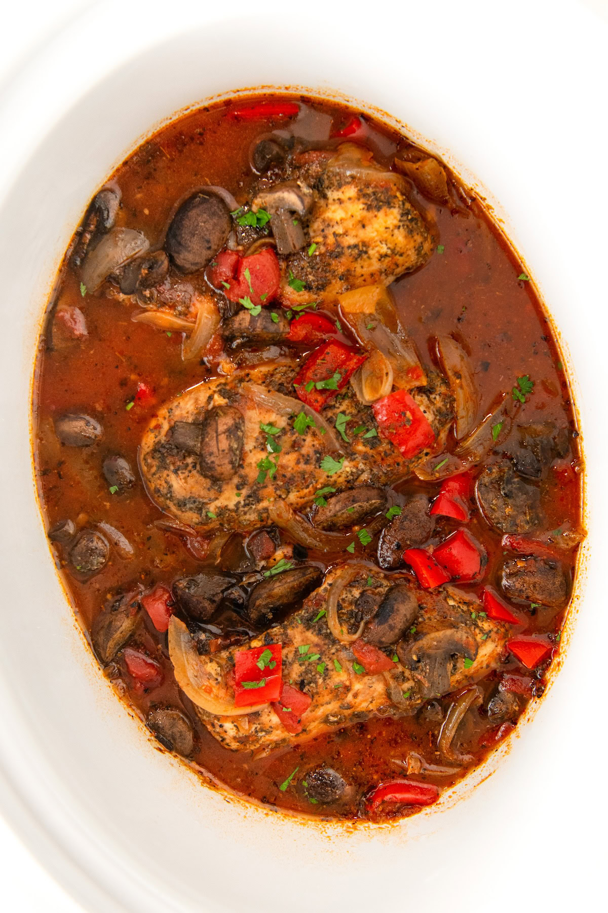 Savory, tender chicken cacciatore is presented in a white crockpot.