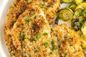 A plate of crispy parmesan crusted chicken and sprouts on a round white plate.