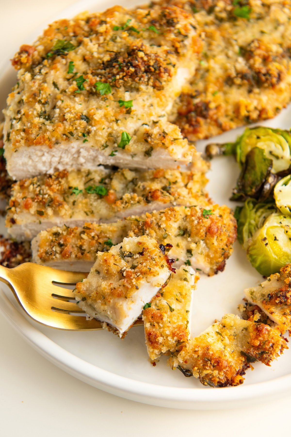 Sliced mayo chicken served with roasted brussels sprouts on a white plate.