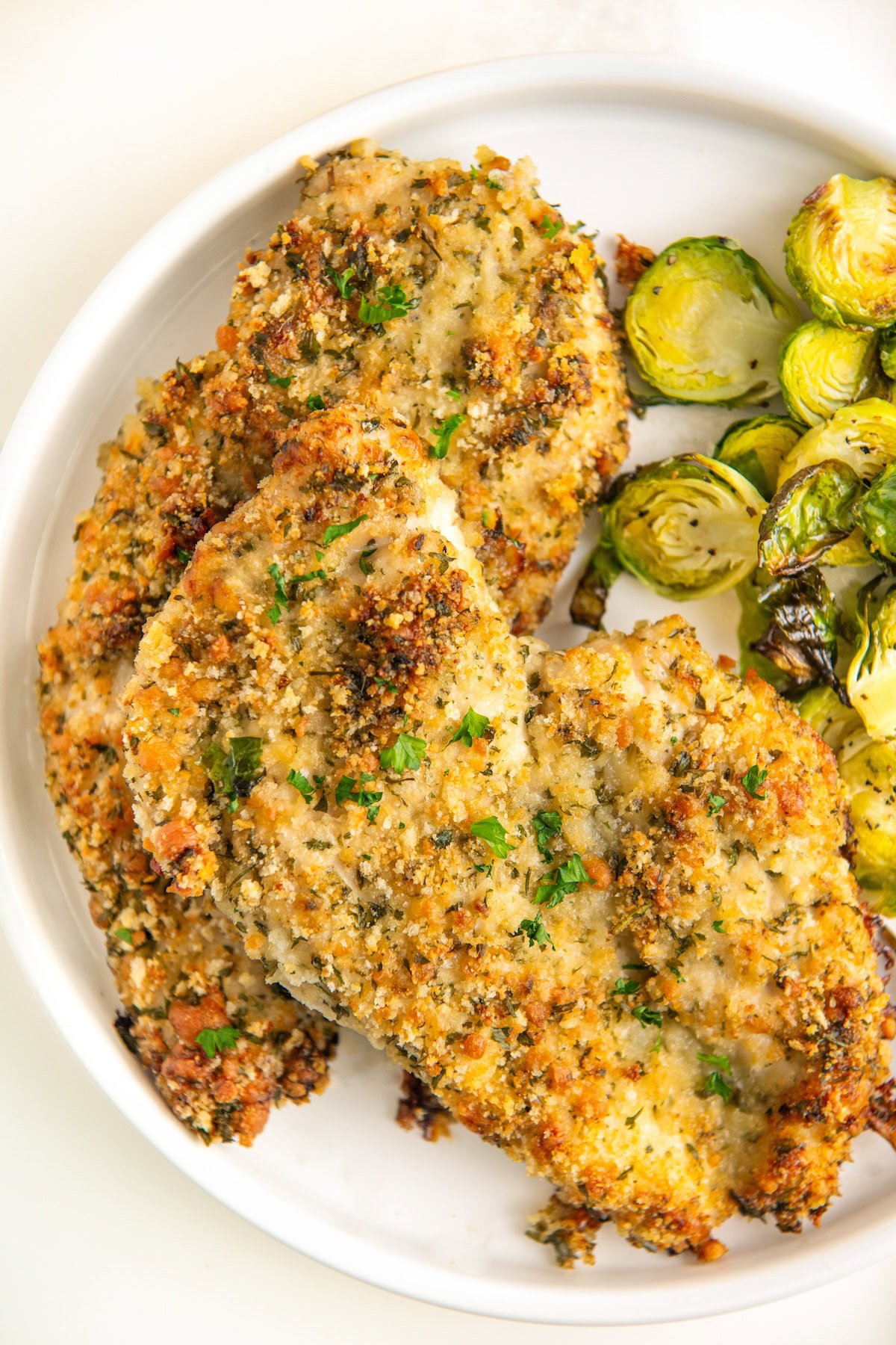 A plate of crispy parmesan crusted chicken and sprouts on a round white plate.