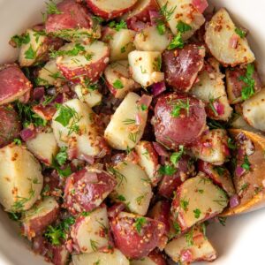 A large white serving bowl is filled with German potato salad.