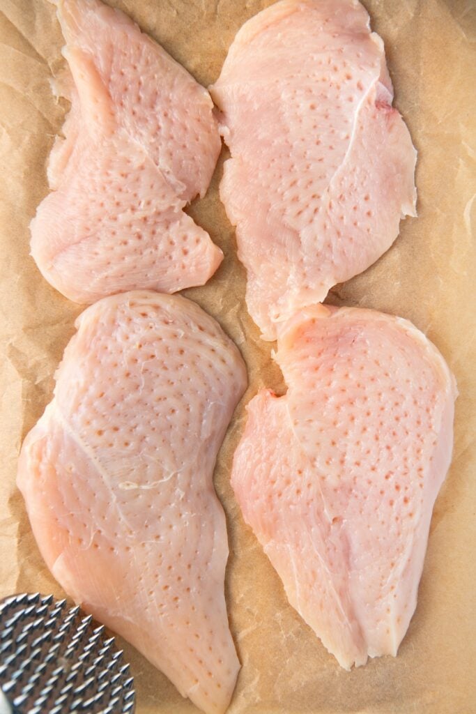 Chicken breast halves are tenderized and presented on a sheet of parchment paper.