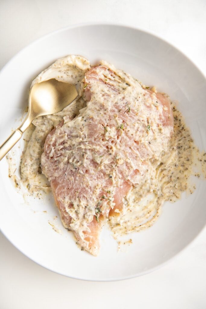 Raw chicken is being coated in seasoned mayo.