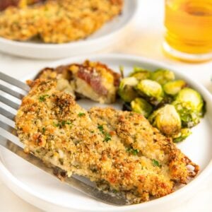 Crispy chicken breast plated beside roasted brussels sprouts.