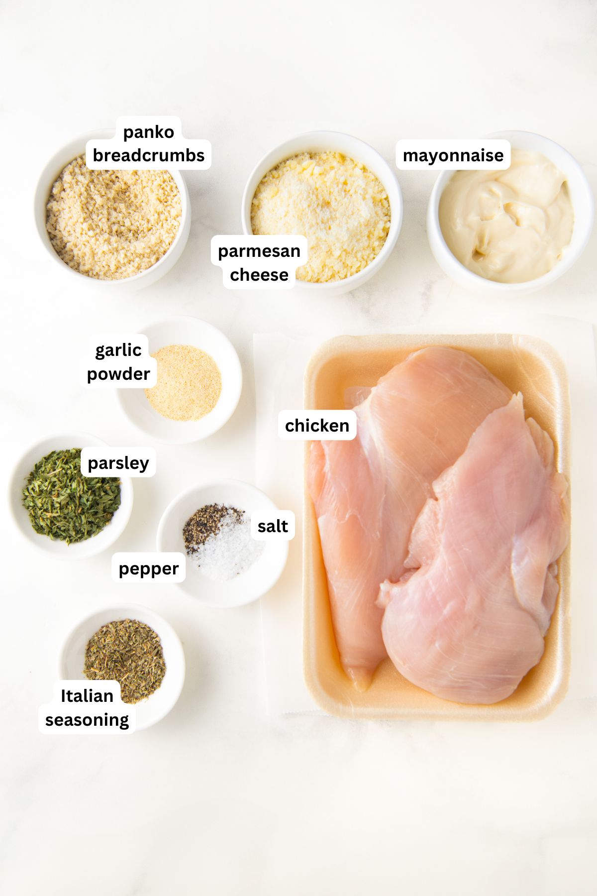 Parmesan crusted chicken recipe ingredients in order from top to bottom: panko breadcrumbs, parmesan cheese, mayonnaise, garlic powder, parsley, pepper, salt, chicken, Italian seasoning.