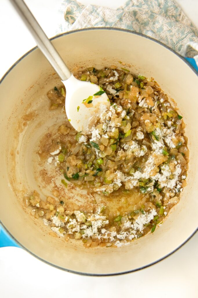 Flour has been stirred into vegetables cooking in a pot.