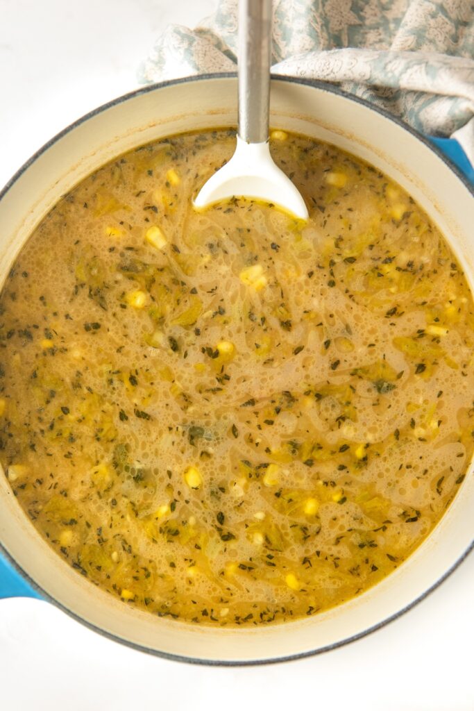 A white spoon is stirring chowder in a pot.
