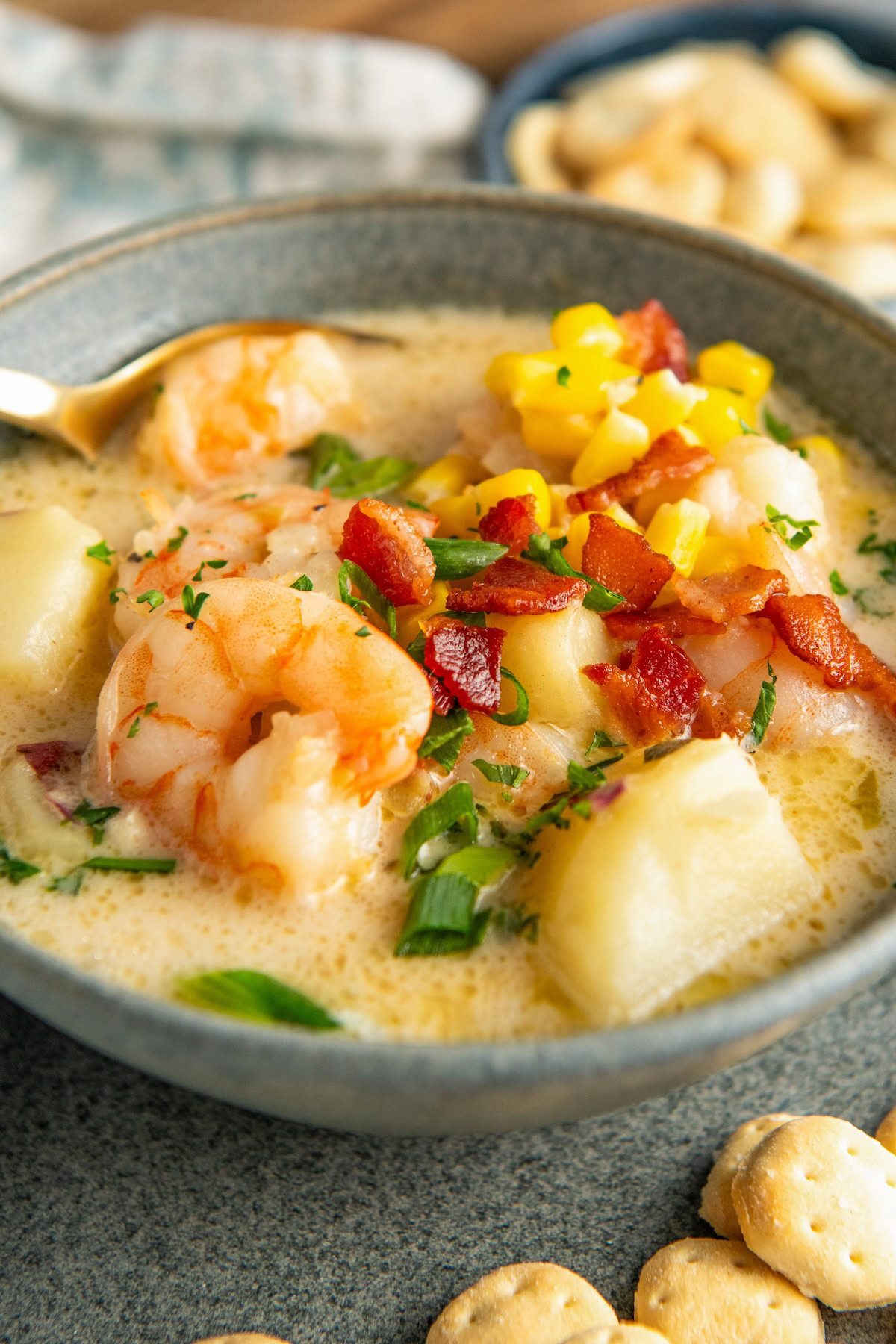 Shrimp, corn, potatoes, and bacon are served in a creamy broth in a bowl.