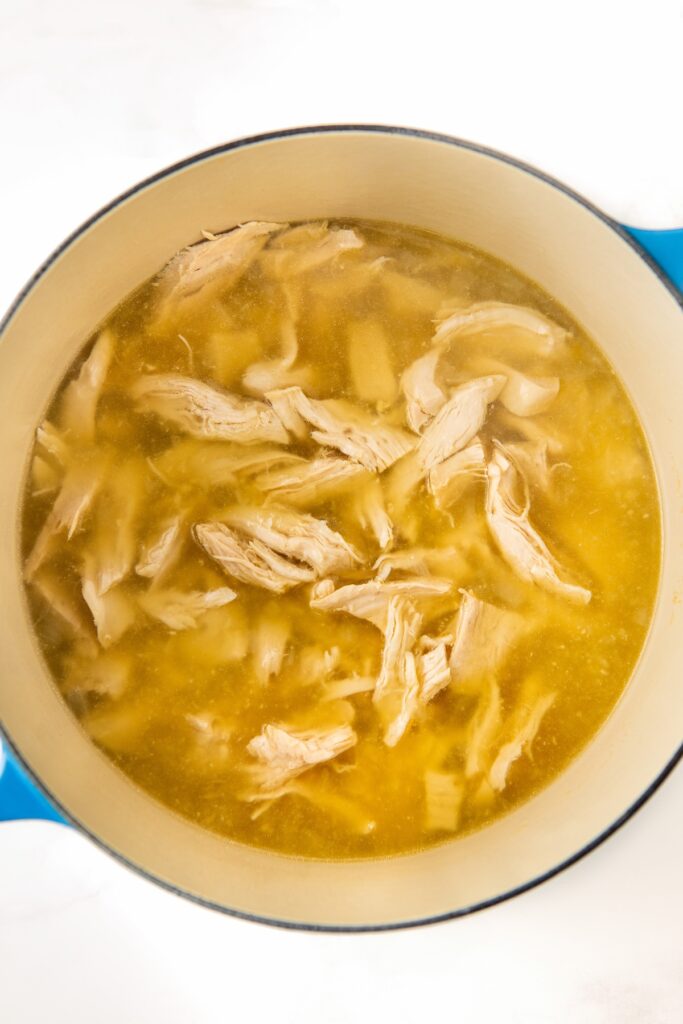 A blue pot filled with shredded chicken pieces submerged in a clear broth.