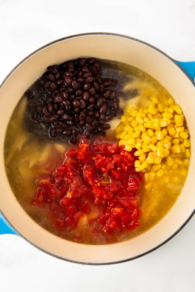 A large pot containing four ingredients in separate sections: black beans, yellow corn, diced tomatoes, and clear broth with shredded chicken.