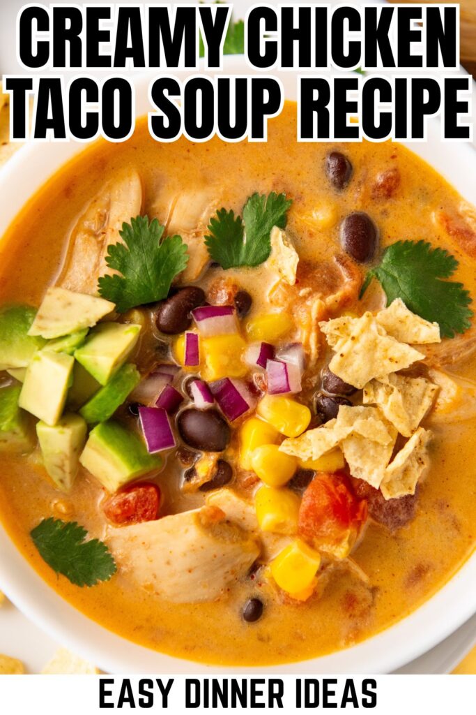 A bowl of creamy chicken taco soup topped with tortilla chips, avocado cubes, black beans, corn, diced tomatoes, and cilantro.