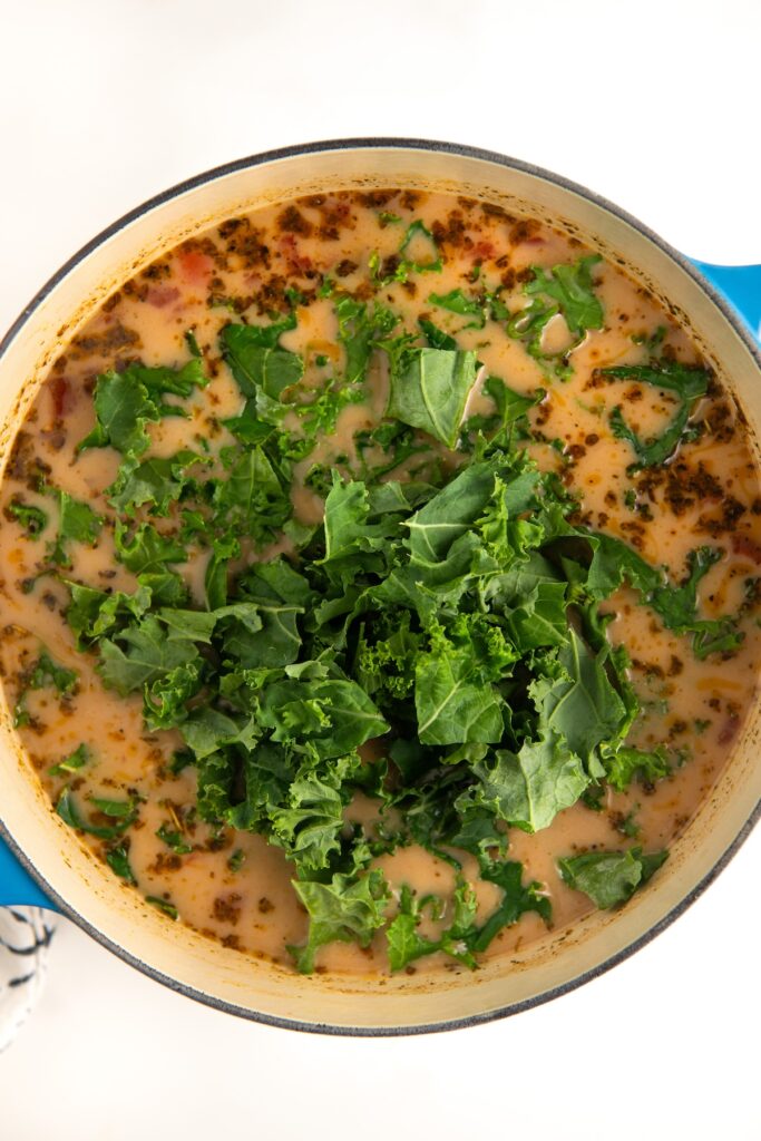 A pot filled with a creamy soup, featuring chopped kale and herbs scattered on top.