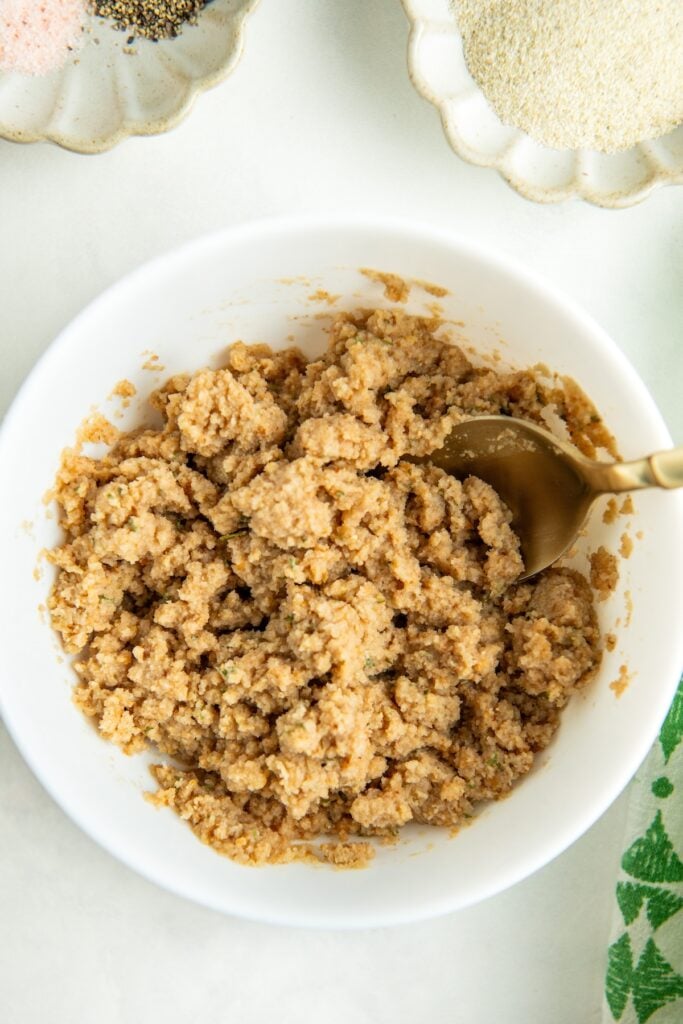 A bowl filled with a crumbly, milk and breadcrumb mixture with a spoon mixing it together.