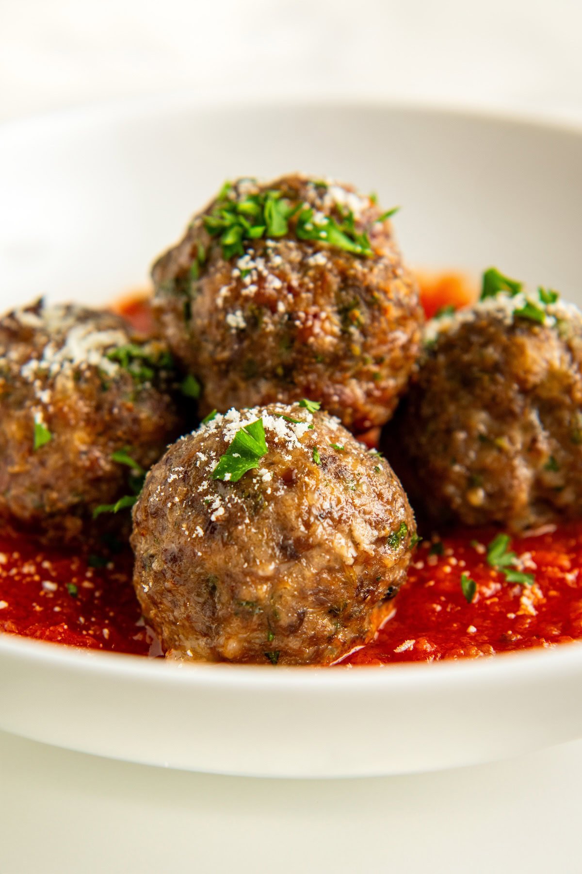 Ready in 30 minutes, this easy Italian meatball recipe uses a secret twist — milk-soaked breadcrumbs — to create the juiciest meatballs, ever! Four baked Italian meatballs garnished with chopped parsley and grated cheese sit on a bed of tomato sauce in a white bowl.