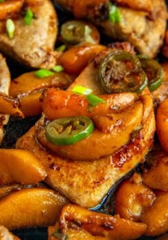 Cooked Jalapeño Peach Pork Chops in a cast iron skillet garnished with green onions, all glistening with a rich, savory sauce.
