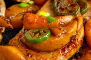 Cooked Jalapeño Peach Pork Chops in a cast iron skillet garnished with green onions, all glistening with a rich, savory sauce.
