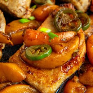 Cooked Jalapeño Peach Pork Chops in a cast iron skillet garnished with green onions, all glistening with a rich, savory sauce.