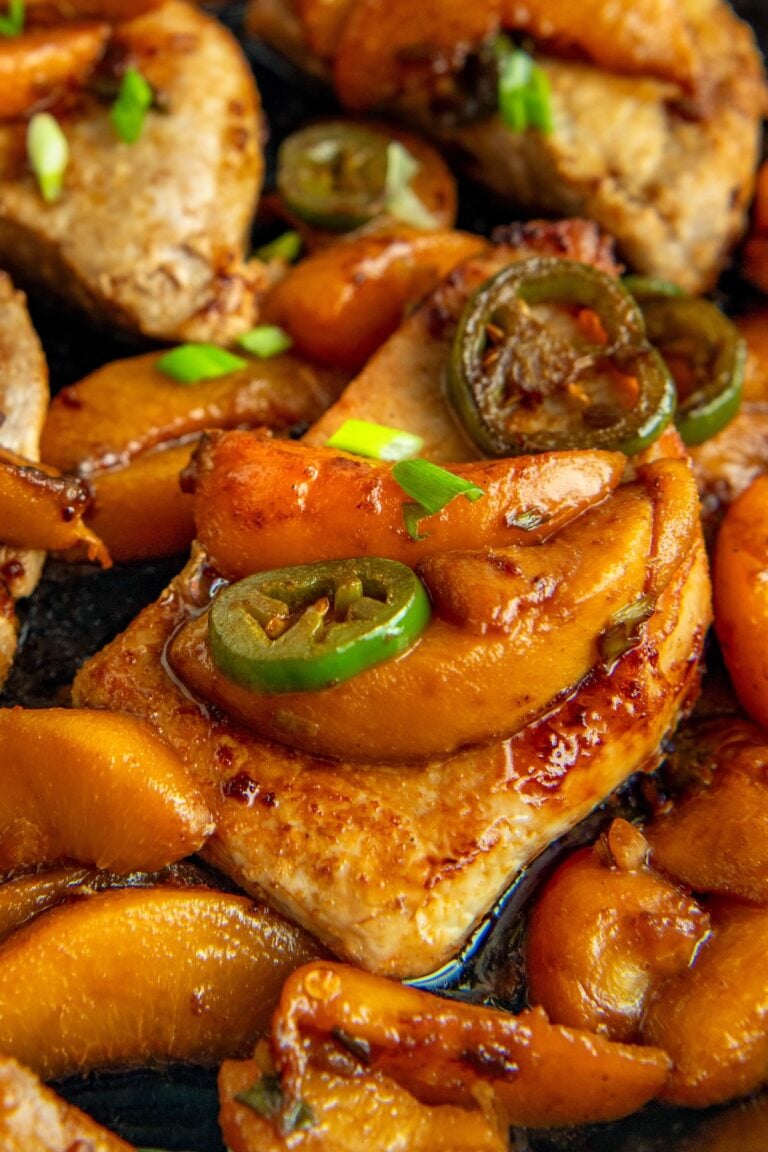 Cooked Jalapeño Peach Pork Chops in a cast iron skillet garnished with green onions, all glistening with a rich, savory sauce.