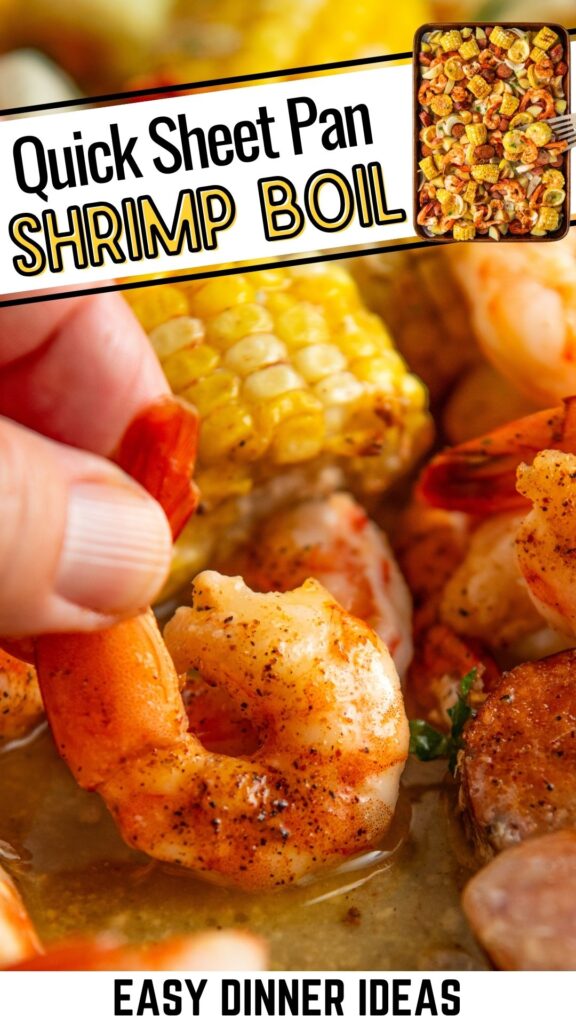 Close-up of seasoned shrimp being picked up by hand, with corn and sausage in the background.