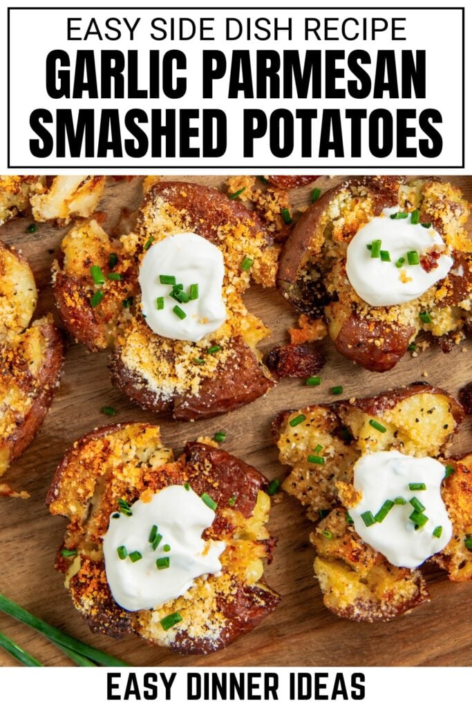 A wooden board topped with crispy garlic smashed potatoes garnished with parmesan, sour cream, and chopped chives.