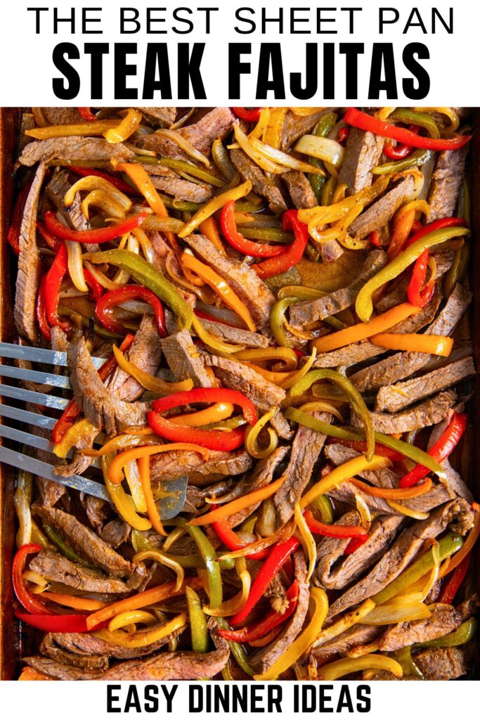 Sheet pan steak fajitas filled with cooked steak strips, red, yellow, and green bell peppers, and onions, with a metal spatula.