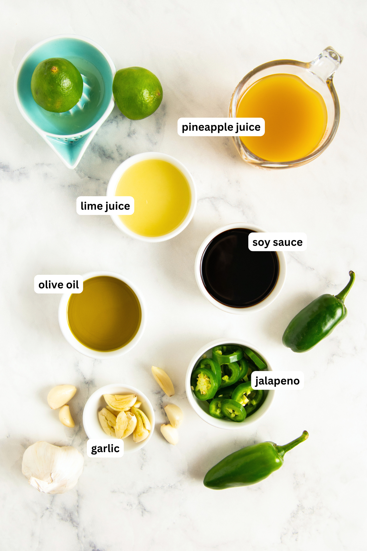 Ingredients for steak fajita marinade arranged on a countertop. From top to bottom: lime wedges, pineapple juice, lime juice, soy sauce, olive oil, jalapeño, and garlic.