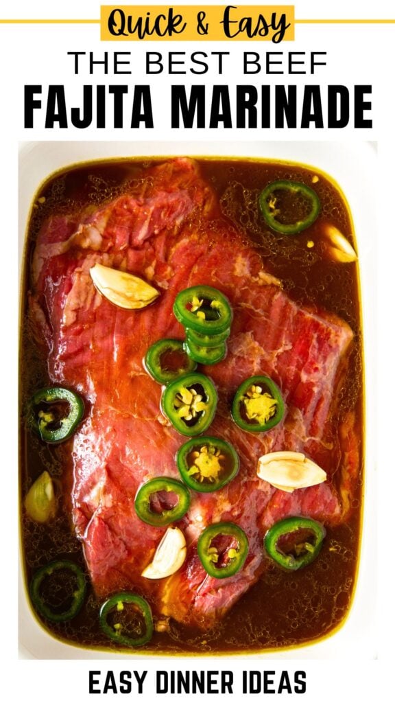 Raw steak marinating in a dish with sliced jalapeños, garlic cloves, and dark liquid marinade.