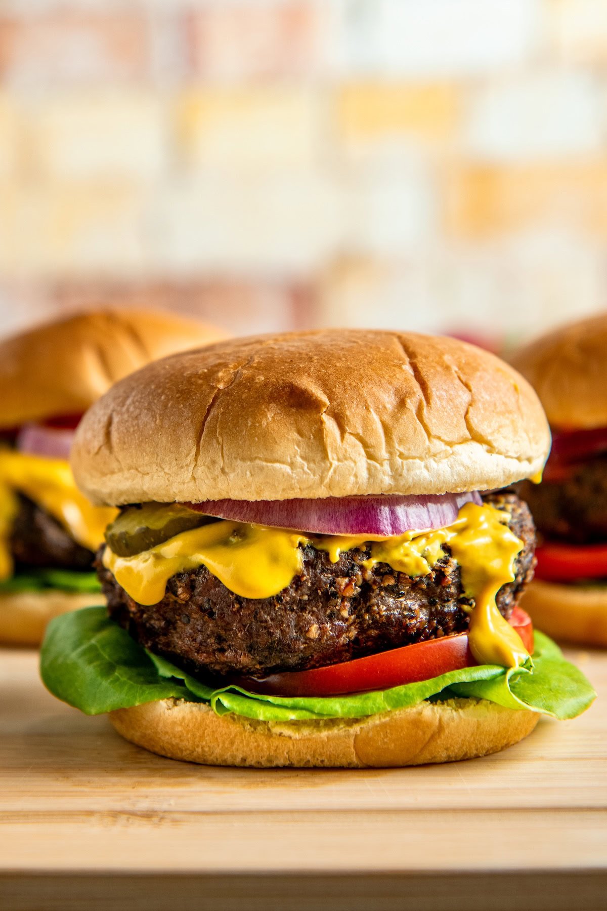 A close-up of a juicy hamburger with a beef patty, lettuce, tomato, pickles, red onion, and mustard, all inside a golden, fluffy bun, sitting on a wooden surface.