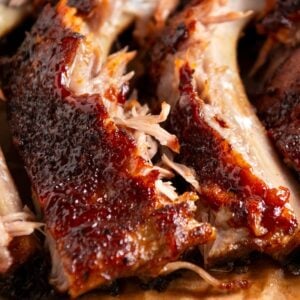 Close-up of juicy, glazed slow cooker baby back ribs with a caramelized crust, arranged on parchment paper, showing tender meat and visible bones.