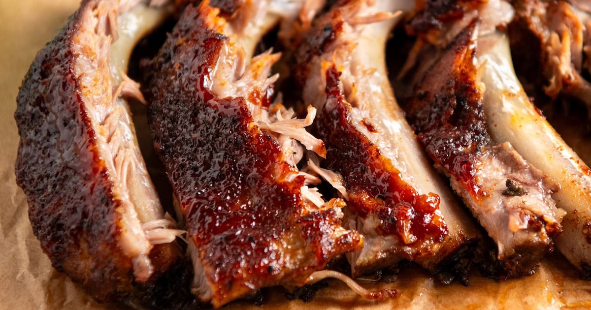 Close-up of juicy, glazed slow cooker baby back ribs with a caramelized crust, arranged on parchment paper, showing tender meat and visible bones.