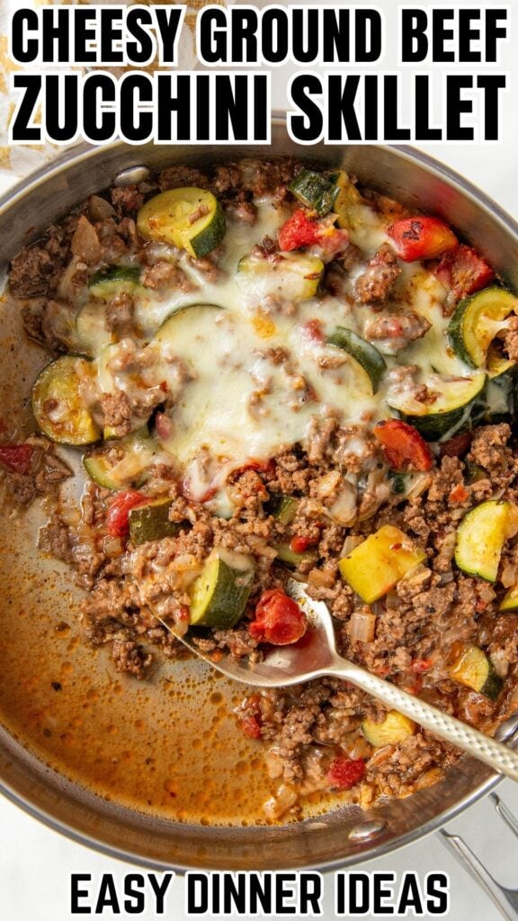 A skillet filled with ground beef, zucchini, tomatoes, and melted cheese, with a spoon resting inside.
