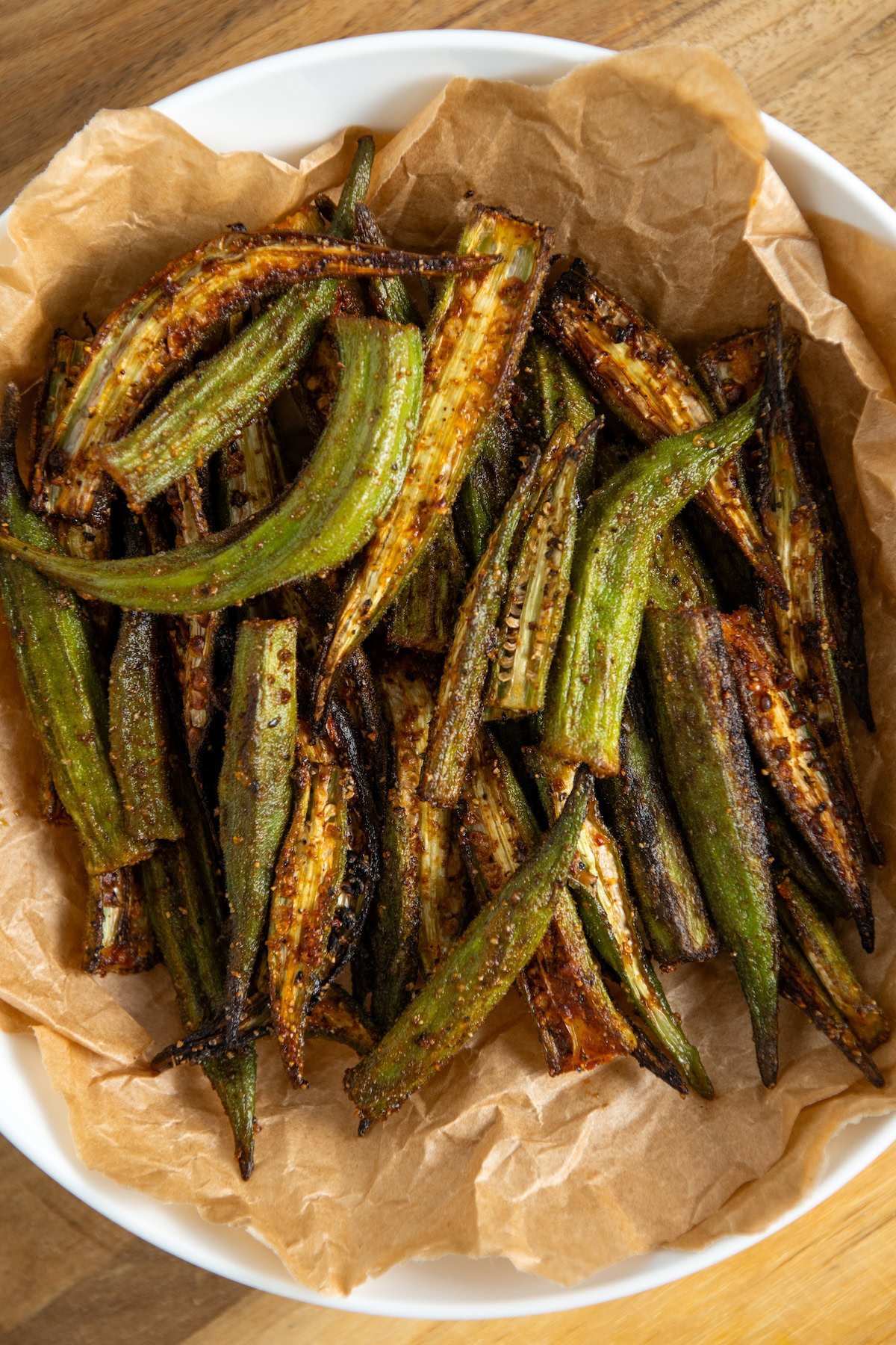 A bowl lined with brown parchment paper filled with air fryer, seasoned and slightly charred, sitting on a wooden surface.