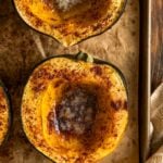 Close-up of two roasted acorn squash halves on a baking sheet, sprinkled with spices and filled with melting butter in the centers.