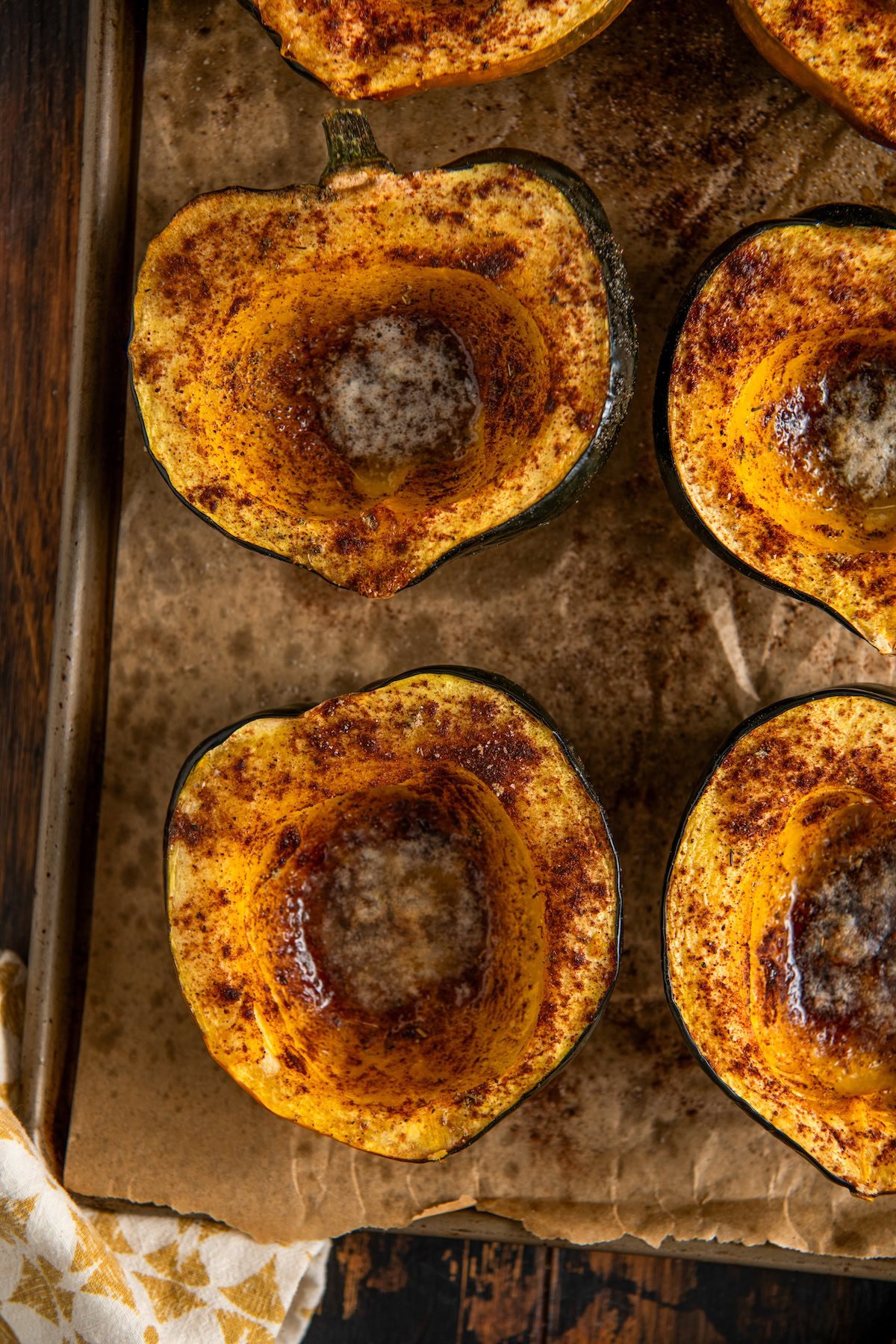 Halved roasted acorn squash on a parchment paper lined baking sheet, sprinkled with cinnamon and spices, with melted butter in the center.