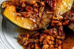 A baked acorn squash half topped with a maple pecans glaze sits on a white plate.