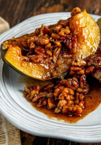 A baked acorn squash half topped with a maple pecans glaze sits on a white plate.