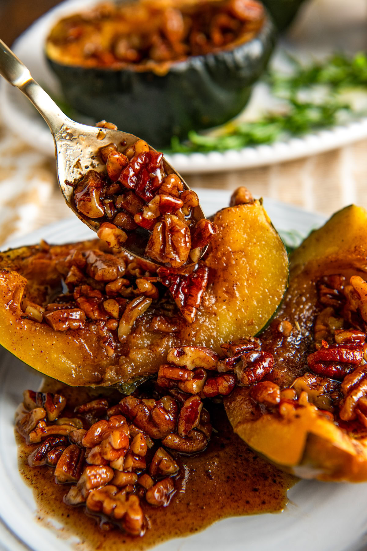 A spoon drizzling baked acorn squash halves with a maple pecan glaze.