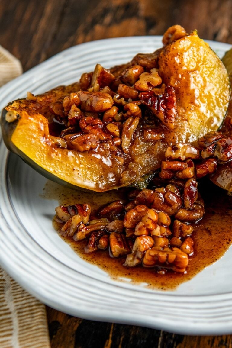 A baked acorn squash half topped with a maple pecans glaze sits on a white plate.