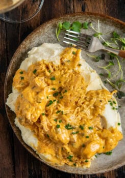 A plate of creamy crockpot French Market chicken and gravy served over mashed potatoes, garnished with chopped chives, with a fork and microgreens on the side.