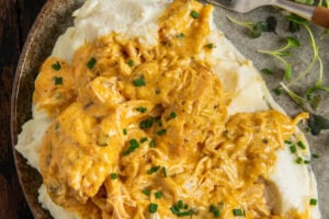 A plate of creamy crockpot French Market chicken and gravy served over mashed potatoes, garnished with chopped chives, with a fork and microgreens on the side.
