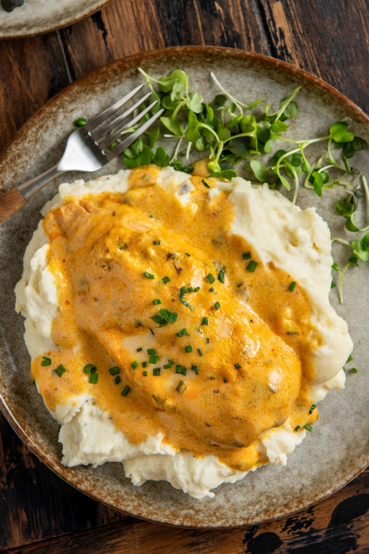 A plate of mashed potatoes with crockpot French Market chicken and chopped chives.